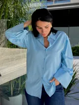 Camisa celeste de manga larga con puños anchos, cuello clásico y cierre frontal abotonado.