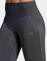 Calza deportiva Adidas Seamless 7/8 de tiro alto, color negro, confeccionada con tejido suave y elástico sin costuras con tecnología AEROREADY. Presenta diseño de líneas acanaladas en la cintura y los tobillos, y las tres tiras características de la marca en el muslo derecho.