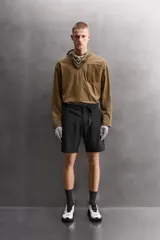 Bermuda de ajuste regular color marrón oscuro, confeccionada en tejido técnico compacto con elasticidad. Presenta cintura ajustable con cinturón negro a contraste, bolsillos frontales y un bolsillo cargo con cierre de cremallera oculta en la pernera.