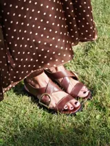 Sandalias de cuero color marrón con tiras anchas cruzadas y hebilla metálica decorativa en forma de estribo. Presentan taco cuadrado de altura media y suela de goma.