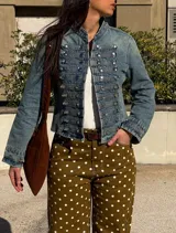 Chaqueta de denim estilo militar, de corte corto, cuello mao y múltiples hileras de botones metálicos frontales.