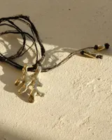 Collar con dije de metal plateado con forma orgánica o de coral, atado a un hilo negro de seda natural o algodón. El collar tiene terminales cilíndricos metálicos en los extremos del hilo ajustable.