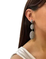 Aros colgantes largos con forma ovalada, recubiertos de hilos brillantes color dorado.