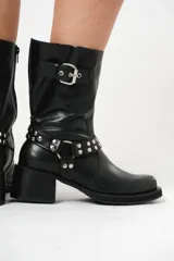 Bota biker de caña media color negro, con hebilla en la parte superior y detalle de aro y tachas en la parte inferior.