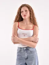 Musculosa blanca de tirantes finos con ribetes rojos, con la palabra "Merci" bordada en rojo y un corazón debajo.