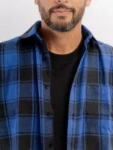 Camisa de franela a cuadros en tonos azul y negro, con cuello clásico, cierre frontal de botones y bolsillo en el pecho.