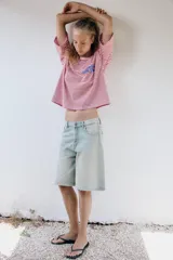 Camiseta oversize de rayas horizontales rojas y blancas, con cuello redondo y mangas cortas. Presenta un estampado de texto azul en el pecho y estrellas azules en las mangas.