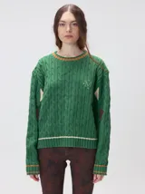 Sweater de punto con diseño de ochos en color verde, cuello redondo con detalle de franja en contraste, y apliques de rombos en las mangas. Presenta un bordado con la letra M en el pecho.