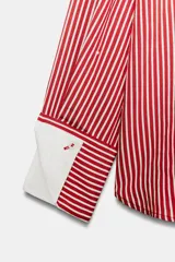 Camisa de cuello solapa y manga larga con rayas verticales rojas y blancas, con puños anchos blancos contrastantes y cierre frontal de botones.