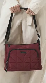 Bandolera de diseño práctico y moderno, confeccionada en tela impermeable color verde militar. Presenta un bolsillo frontal con diseño capitoneado geométrico, cierre principal y bolsillo trasero con cierre. Incluye correa ajustable y detalles en negro.