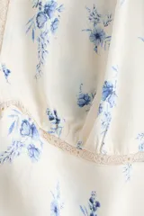 Vestido maxi de viscosa color marfil con estampado floral azul, escote en V pronunciado con ribete de encaje, mangas largas abullonadas y corte entallado.