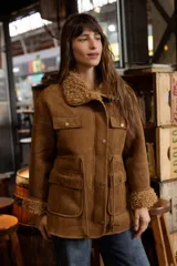 Campera de efecto gamuza color tostado con interior de corderito sintético. Presenta cierre frontal, bolsillos delanteros con solapa, cintura ajustable con cordón y puños con detalle de corderito.