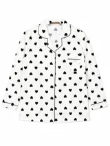 Camisa de pijama de manga larga con cuello solapa, cierre frontal de botones y bolsillo en el pecho. Presenta un estampado de corazones negros sobre fondo blanco y detalles de ribetes negros en cuello, puños y bolsillo.