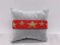 Pulsera tejida con pequeñas cuentas de colores rojo y dorado, formando un patrón de estrellas doradas sobre fondo rojo.