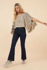 Poncho color beige con diseño a cuadros, cuello bote y terminaciones desflecadas. Tiene aberturas para los brazos en los laterales y detalles en cuero.