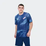 Remera deportiva Umbro modelo Press, de color rojo con un estampado abstracto en tonos más oscuros, cuello redondo y manga corta. Incluye el logo de la marca en el pecho y el escudo del Club Nacional de Football.