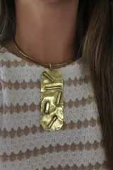 Gargantilla dorada con dije rectangular texturizado con apliques de barras horizontales y verticales.