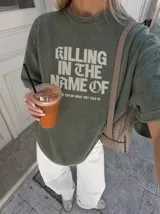 Remera gris con efecto acid wash y diseño oversize. Presenta un estampado frontal con la inscripción "KILLING IN THE NAME OF" y la frase "NOW YOU DO WHAT THEY TOLD YA".
