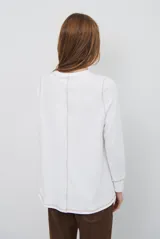 Remera de manga larga en color beige, confeccionada en tejido de punto con costuras a la vista en contraste. Presenta un corte holgado, cuello redondo y un pequeño bordado distintivo en la parte inferior.