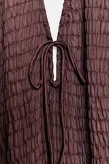 Vestido midi color marrón oscuro o ciruela, con escote halter y detalle de tejido fruncido con elásticos y lazada en el busto. La falda es fluida y plisada.