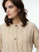 Cárdigan de punto con diseño de ochos, color beige, con cuello redondo, cierre frontal de botones tipo carey y puños acanalados.