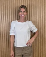 Blusa blanca de corte recto con escote a la base y mangas cortas abullonadas con terminación fruncida.
