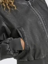 Chaqueta bomber corta de cuero sintético efecto gastado en color negro, con cuello redondo, cierre frontal de cremallera, bolsillos ribeteados y puños y cintura acanalados.