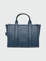 Cartera tipo tote de cuero granulado color tostado, con diseño estructurado y rectangular. Presenta doble asa superior fija y una correa larga ajustable y extraíble. En el frente, destaca el logo estampado con la inscripción 'THE TOTE BAG MARC JACOBS'.