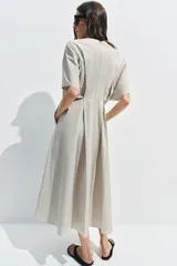 Vestido midi de popelín de algodón en color beige, con cuello redondo, manga corta y pliegues en la cintura. Presenta una falda en línea evasé y cierre en la espalda con cremallera oculta.
