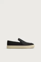 Mocasín casual de cuero negro con textura granulada, diseño sin cordones y suela de goma a contraste en color beige.