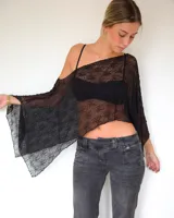 Capa de encaje negro con diseño asimétrico y caída holgada, ideal para usar sobre otras prendas.