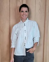 Camisa de algodón a rayas verticales blancas y azules, con cuello alto tipo gorguera con volados, cierre frontal de botones y mangas largas con puños con volados.