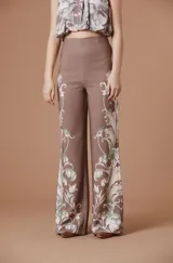 Pantalón de tiro alto con silueta amplia y corte recto, confeccionado en tela fluida color marrón con estampado botánico en tonos claros en los laterales.