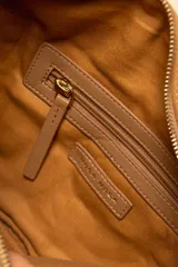 Bandolera de gamuza color marrón con diseño de media luna, decorada con tachas metálicas doradas distribuidas en el frente. Cuenta con cierre superior metálico y correa larga ajustable para llevar cruzada.