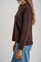 Sweater de tejido de punto liso, color marrón oscuro, con cuello redondo y calce oversize. Presenta detalles de costura en diagonal en la parte inferior delantera.