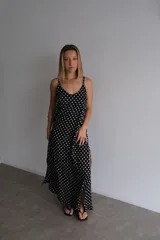 Vestido largo de crepe con estampado de lunares negros sobre fondo blanco. Presenta un diseño de corte holgado con breteles finos y escote redondeado.