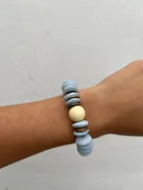 Set de tres pulseras elásticas con cuentas de madera en colores celeste, negro y rosa, con detalles de cuentas doradas y cuentas color crema.