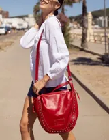 Cartera de cuero roja con tachas plateadas en el borde inferior, doble asa de cuero y cierre superior.