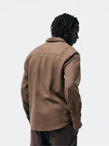 Camisa de manga larga en color gris, con cuello clásico, cierre frontal de botones y un bolsillo en el pecho.