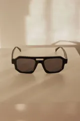 Lentes de sol con armazón grueso de policarbonato en color negro, de forma geométrica y cristales oscuros. Cuentan con protección UV400 y un detalle metálico plateado en el puente.