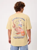 Remera Rusty de corte holgado, color amarillo, con estampa en la espalda de un personaje surfeando sobre un pez y textos descriptivos.