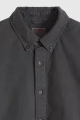 Camisa de manga larga color negro lavado, con cuello camisero con botones y cierre frontal abotonado.
