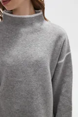 Polera de tejido de punto color negro con detalles de vivos en color beige en el cuello, puños, ruedo y costuras de las mangas. Presenta un diseño holgado con cuello alto y mangas largas.