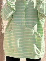 Canguro oversize de rústico de algodón con diseño a rayas horizontales en color verde menta y blanco. Presenta capucha, escote con broches frontales, bolsillo tipo canguro al frente y puños elásticos en mangas y ruedo.