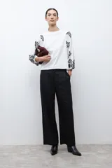 Remera de color crudo con mangas largas abullonadas, decoradas con bordados en color negro. Presenta un diseño de cuello redondo y corte recto.