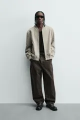 Cazadora bomber negra de corte regular fit, confeccionada en tejido efecto ante. Cuenta con cuello, puños y bajo en rib elástico, manga larga, bolsillos de vivo en la cadera y un bolsillo interior. Cierre frontal con cremallera.