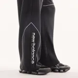 Pantalón de jogging New Balance Trackside negro de corte recto y holgado, con cintura elástica con cordón ajustable, bolsillos laterales y líneas de ribete blancas en contraste. Cuenta con un pequeño logo bordado en la pierna.