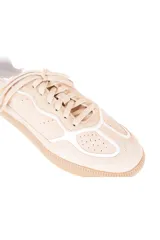 Championes de estilo urbano con diseño inspirado en el calzado deportivo vintage. Están confeccionados en una combinación de cuero vacuno y gamuza en tonos neutros, con suela plana de goma en color caramelo y detalles en blanco.
