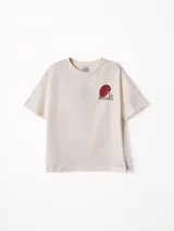Remera de algodón color beige con diseño de cuello redondo y pequeño estampado en el pecho. Presenta un corte holgado y mangas cortas.