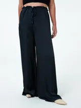 Pantalón negro de tela satinada, corte palazzo, cintura alta con elástico y lazo ajustable.